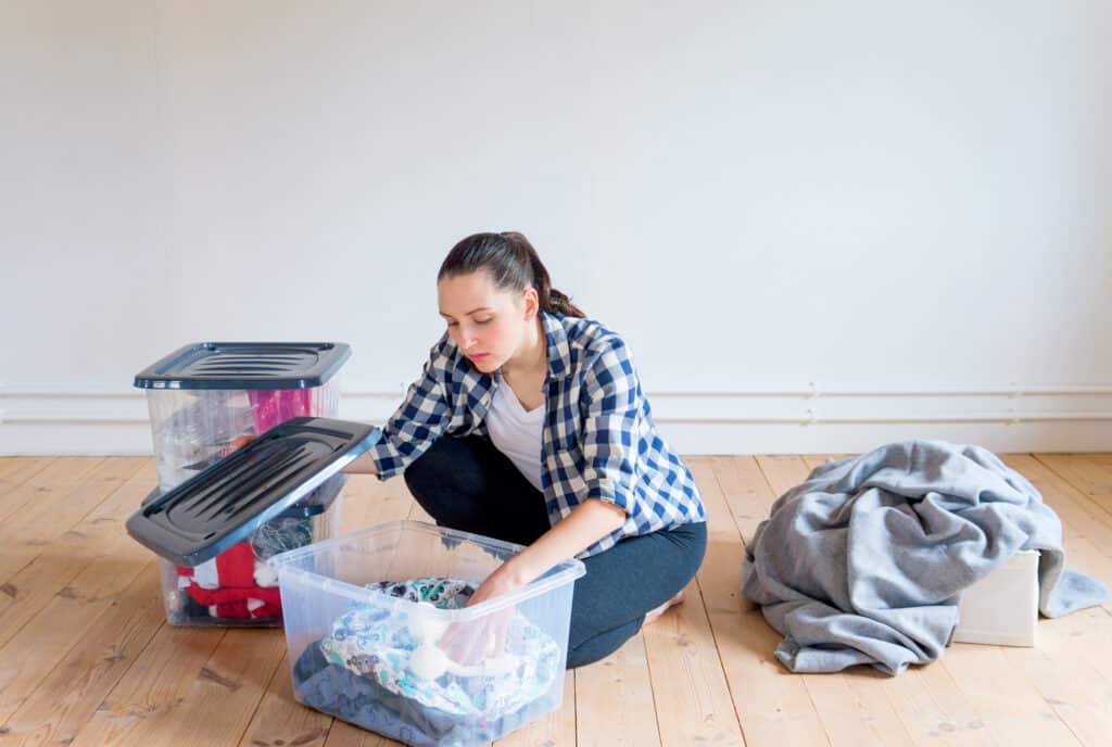 woman putting away clothes in a clear bin in her home